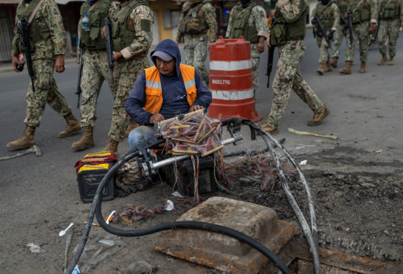 oldados marchan por Durán, Ecuador, mientras un trabajador repara cables de internet. Crédito: Associated Press