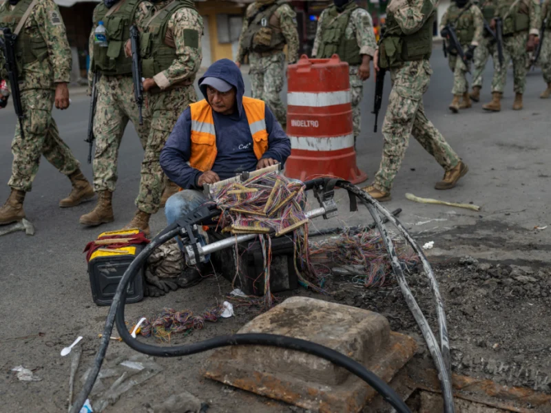 oldados marchan por Durán, Ecuador, mientras un trabajador repara cables de internet. Crédito: Associated Press