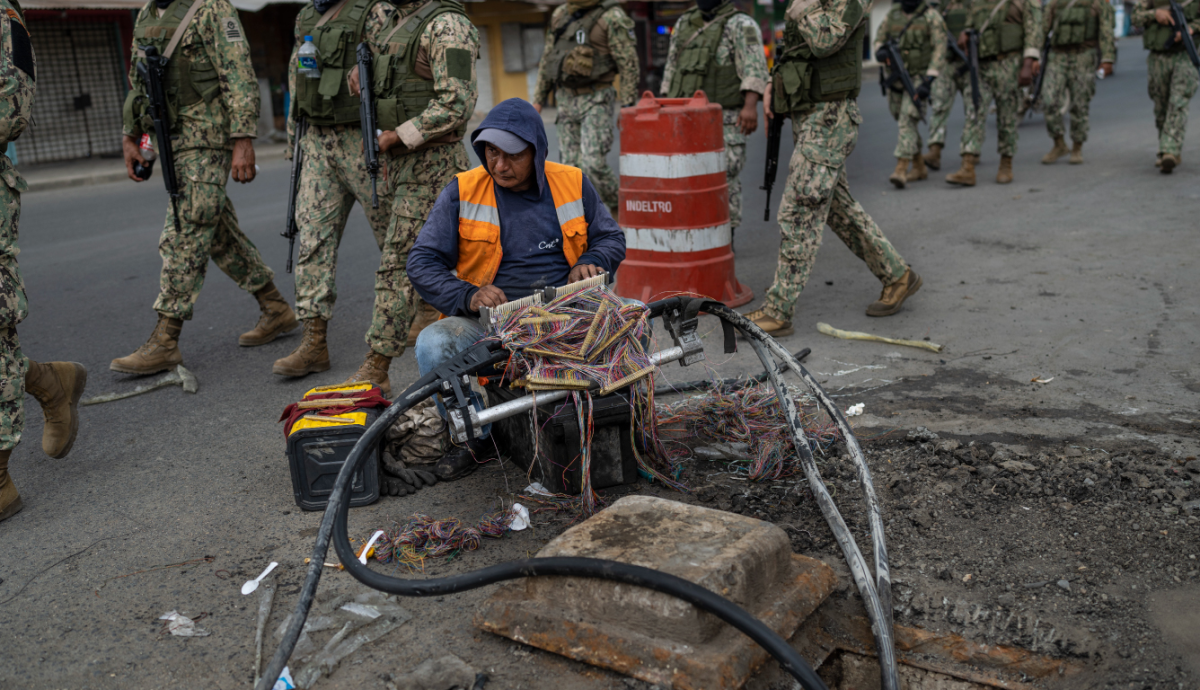 oldados marchan por Durán, Ecuador, mientras un trabajador repara cables de internet. Crédito: Associated Press